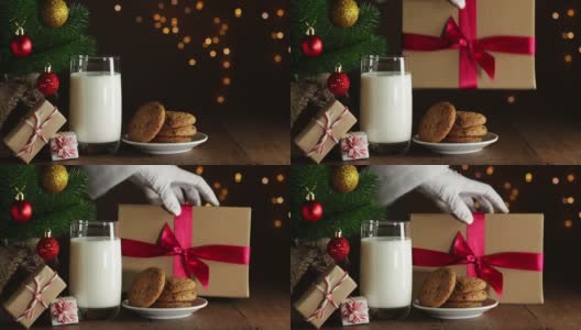 在圣诞树上放牛奶和饼干。圣诞老人手把带红丝带的礼盒放在木桌上高清在线视频素材下载