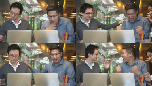 4K视频的亚洲商人在休闲西装工作笔记本电脑在现代的工作场所或咖啡店与同事，而他的成功来了，并祝贺一起，商业和自由职业者的概念高清在线视频素材下载
