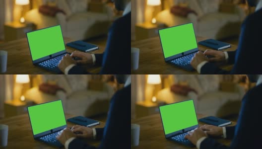 在家的男人坐在他的桌子上，在绿色屏幕的笔记本电脑上打字。他的公寓是黄色的，很温暖。高清在线视频素材下载