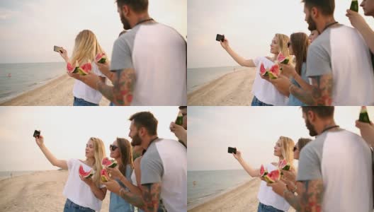 朋友们站在沙滩上吃西瓜，用智能手机相机自拍。年轻的男人和女人穿着蓝色的牛仔裤短裤在海边聊天。健康营养，素食高清在线视频素材下载