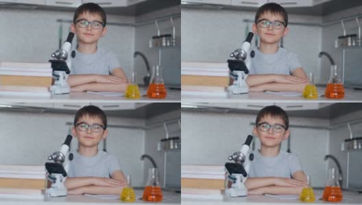 一个男生坐在厨房里的显微镜和课本旁边，看着摄像机微笑着高清在线视频素材下载