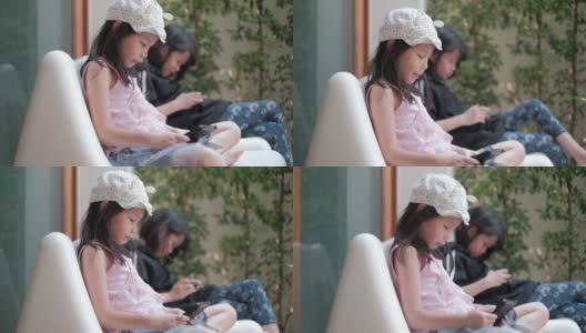 旁边拍摄的画面:两个泰国籍的亚洲女孩穿着休闲服装，专注于玩手机和平板电脑上的网络游戏。白天在花园区内。高清在线视频素材下载