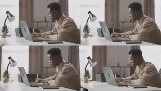 一名黑人青年在笔记本电脑上观看和收听在线学习研讨会，在家通过网络自学，做笔记高清在线视频素材下载