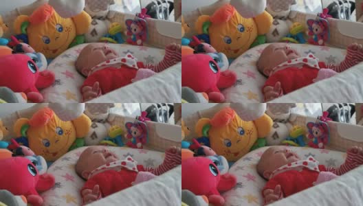 微笑的婴儿看着她的玩具，笑着看着玩具旋转。三个月大的女婴在床上玩耍。COVID-19大流行期间的新生儿。高清在线视频素材下载
