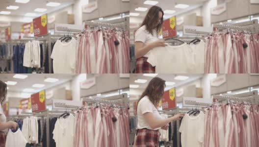 一位年轻的妇女在商店里挑选衣服高清在线视频素材下载