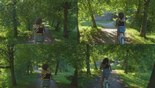 一位女艺术家在阳光下骑着自行车穿过绿色的小巷，享受生活高清在线视频素材下载