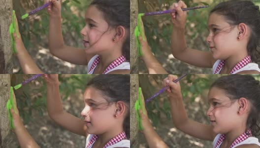 快乐的小女孩在夏令营用手在树上画记号，在外面的艺术，孩子们在户外的公园里玩树下的慢镜头高清在线视频素材下载