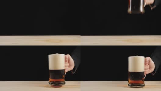 新鲜的啤酒。手把一杯美味的手工啤酒放在啤酒杯里，放在一张黑色背景的木桌上。冰凉的新鲜啤酒，带有水滴，泡沫和泡沫。4 k高清在线视频素材下载