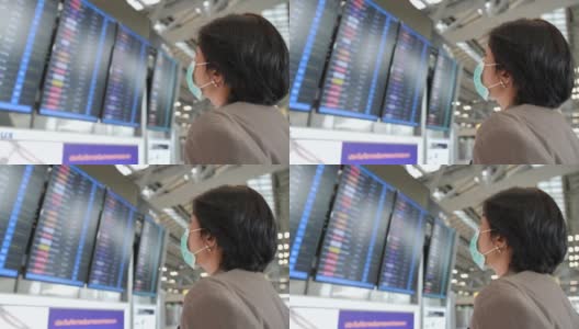 一名亚洲妇女戴着防毒面具看屏幕查看航班。高清在线视频素材下载