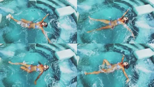 顶部的观点美丽的年轻女子在比基尼和太阳镜放松在游泳池在水晶清澈的水。缓慢的运动。1920 x1080高清在线视频素材下载