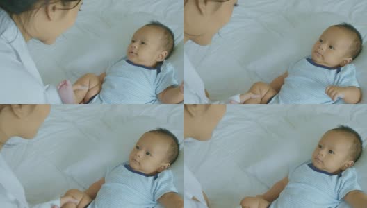 年轻的亚洲母亲与躺在床上的婴儿儿子玩耍。高清在线视频素材下载