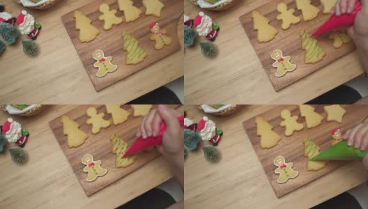 特写镜头:人的手用绿色糖霜来准备，装饰糖霜画体自制的圣诞树饼干、姜饼、圣诞树在木制圣诞桌子上。一些饼干在一个木盘子里高清在线视频素材下载
