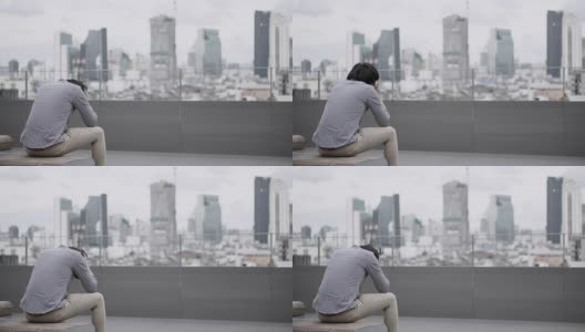 年轻的亚洲商人感到压力和沮丧的工作和生活问题坐在办公大楼屋顶露台的长凳上。背景中的城市视图。重度抑郁症的概念。高清在线视频素材下载