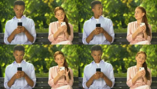 男女青少年坐在长椅上，用智能手机聊天，问题高清在线视频素材下载