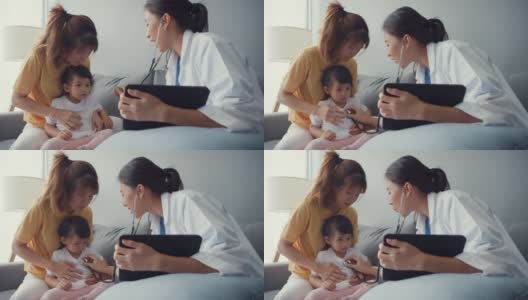 亚细亚女儿科医生拿着听诊器检查小女孩病人和妈妈坐在家里客厅的沙发上看医生。高清在线视频素材下载