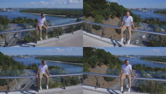 跟踪拍摄一个人坐在玻璃桥的栏杆上，以城市为背景。一个白人坐在一根狭窄的金属管上。失去希望和自杀的概念。总会有出路的高清在线视频素材下载