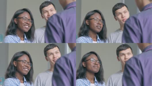 两个大学生，非洲女孩和亚洲男孩向面熟的老师提问，在休息中听他的回答，并被他的笑话逗乐高清在线视频素材下载