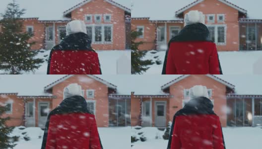 一个冬日，年轻漂亮的红衣女子回家。她穿过后院，走进她那田园诗般的房子。雪花飘落。高清在线视频素材下载