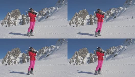 女人拿着滑雪板在她的肩膀上，背景滑雪者滑雪在山区度假胜地高清在线视频素材下载
