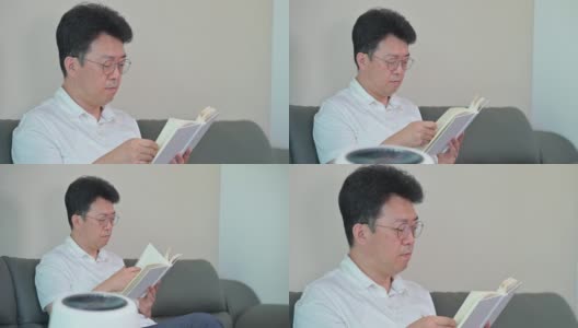 一位亚洲中年男子正在客厅里用空气净化器看书。高清在线视频素材下载