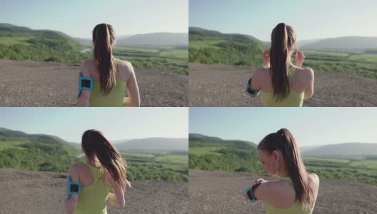 后面的观点。运动员女孩在日落时在山上慢跑，通过摄像头跑步，用智能手机听音乐。女运动员在晚间跑步训练时听音乐。健康的生活方式高清在线视频素材下载