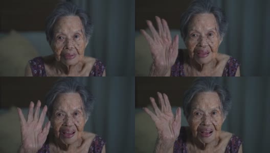 在家里的客厅里，一位年长的亚洲妇女对着照相机微笑和挥手。老年，姿态和人的观念高清在线视频素材下载