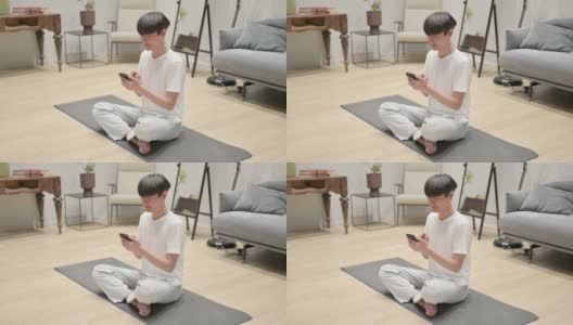 年轻的亚洲男子在瑜伽垫上使用智能手机高清在线视频素材下载
