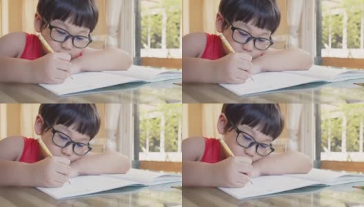 可爱伶俐的小男孩在家里坐在书桌前学习，学生在作业本上写作业，教育观念高清在线视频素材下载