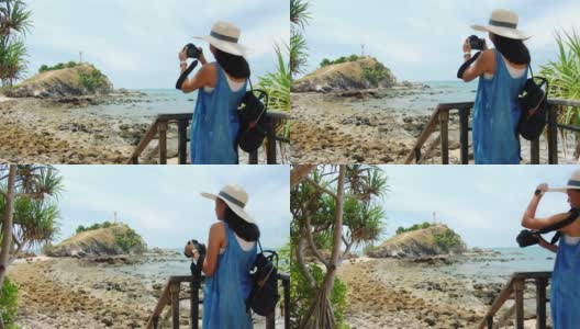 周末度假时，亚洲美女会在以灯塔为背景的海边沙滩上用相机拍照。快乐独自旅行的概念。4 k慢动作。高清在线视频素材下载