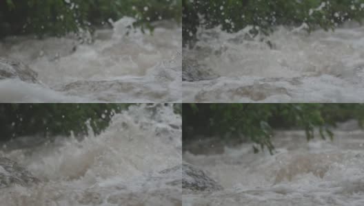 一场瓢泼大雨弄湿了河岸上的植被后，山河湍急地奔流，带着泡沫和溅水的急流跳过岩石高清在线视频素材下载