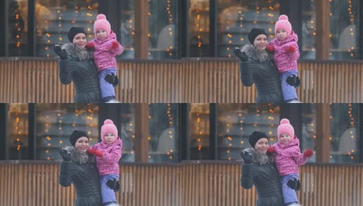 妈妈和她的女儿在冬天的街道上挥舞着他们的手，女人抱着女孩在她的怀里高清在线视频素材下载
