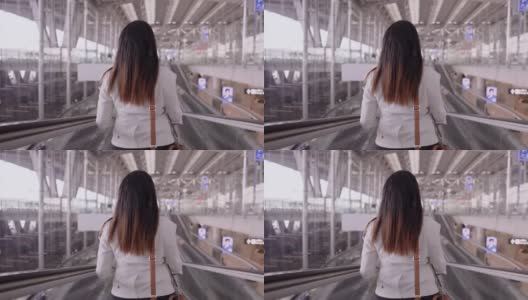女商人在机场往前走，亚洲女商人，在机场做生意带着行李和肩袋在自动扶梯上，手持后视镜高清在线视频素材下载
