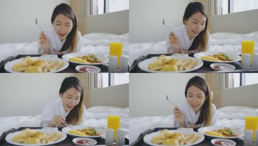 画像美丽的年轻亚洲女人穿着浴袍享受早餐在卧室的床上高清在线视频素材下载