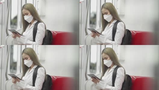 戴着防护口罩的年轻女子在地铁上使用电子平板电脑高清在线视频素材下载
