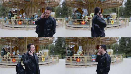 一个年轻人在城市公园里讲手机，背景是一个旋转木马高清在线视频素材下载