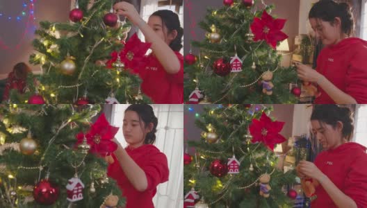 在圣诞节期间，在家里的客厅里装饰圣诞树。美女挂红球。高清在线视频素材下载