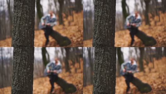 秋天的森林和树在前景和模糊的音乐家弹奏吉他在背景。高清在线视频素材下载
