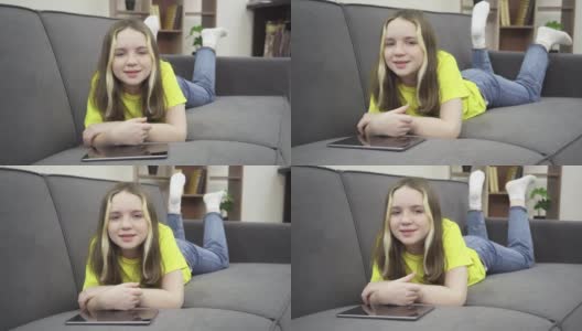 一个小女孩拿着平板电脑躺在沙发上，面带微笑。高清在线视频素材下载