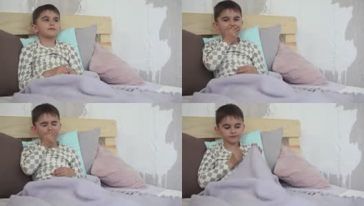 生病的小男孩坐在床上，用毯子盖住自己，咳嗽高清在线视频素材下载