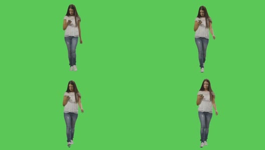 一个休闲的黑发女性正在走路，在绿色屏幕的背景上使用智能手机。高清在线视频素材下载