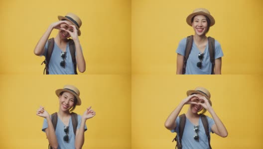 快乐青春美丽亚洲女人旅行者戴帽子和背包显示迷你心与双手爱的标志微笑看着相机在黄色背景。高清在线视频素材下载