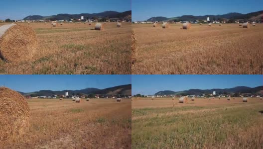 在有圆草堆的田野上空低空飞行。风景如画的小村庄和山峦为背景。高清在线视频素材下载