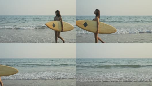在阳光明媚的早晨，年轻的女子拿着冲浪板在海滩上与大海散步。高清在线视频素材下载