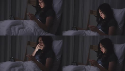 一名亚洲年轻女子晚上躺在床上玩智能手机，在卧室熄灯。在手机上阅读社交。在昏暗的光线下使用手机对眼睛有健康影响。失眠的概念高清在线视频素材下载