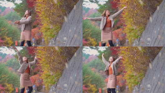 慢动作的微笑年轻美丽的亚洲女子游客扔红色枫叶在秋天的公园。快乐漂亮的女孩，放松和享受美丽的自然。日本旅游度假和秋季季节改变概念。高清在线视频素材下载