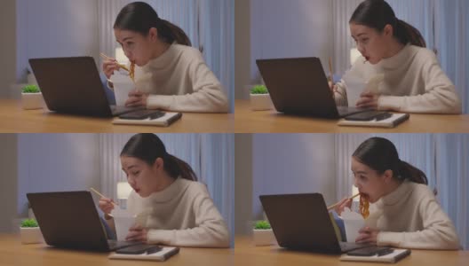 年轻迷人美丽的亚洲女性饿吃方便面中国食品盒带走满嘴看电脑笔记本在家里在忙工作从家里深夜多任务不健康的饮食。高清在线视频素材下载