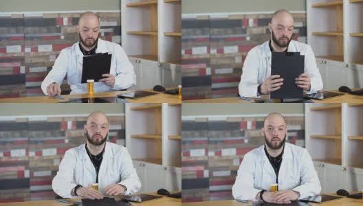 一个30岁的秃顶胡子医生坐在他的医疗室办公室里，在一张全高清的桌子中间高清在线视频素材下载