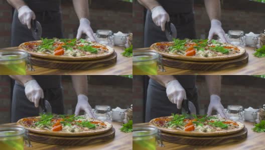 厨师厨师在披萨店的木桌上用滚筒刀切披萨。在意大利餐厅切热披萨切片。制作传统意大利食品的过程。食品的概念高清在线视频素材下载