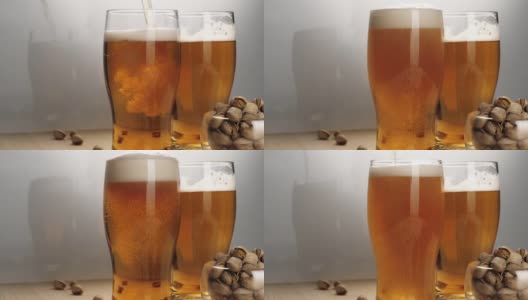 新鲜的啤酒。手在白色背景的木桌上，把美味的冰镇啤酒倒进啤酒玻璃杯里，再放上一些开心果。冰凉的新鲜啤酒，带有水滴，泡沫和泡沫。中间。4 k高清在线视频素材下载