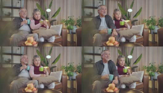 老退休的老亚洲夫妇在家里看电视，老成熟的亚洲夫妇一起在客厅的沙发沙发上欢笑胜利的体育比赛助威活动高清在线视频素材下载